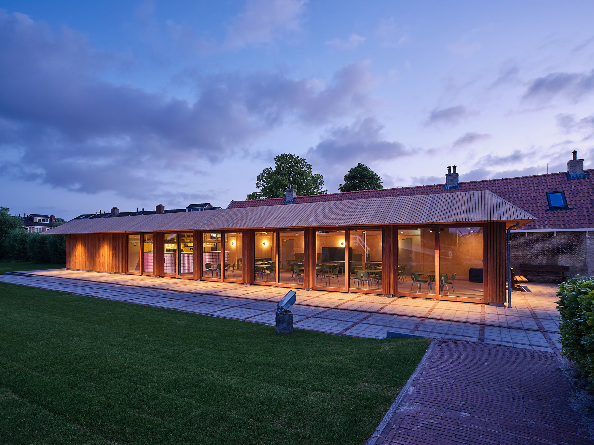 Verlicht houten paviljoen van Het Molenhuis in de schemering, met terras en uitzicht naar binnen