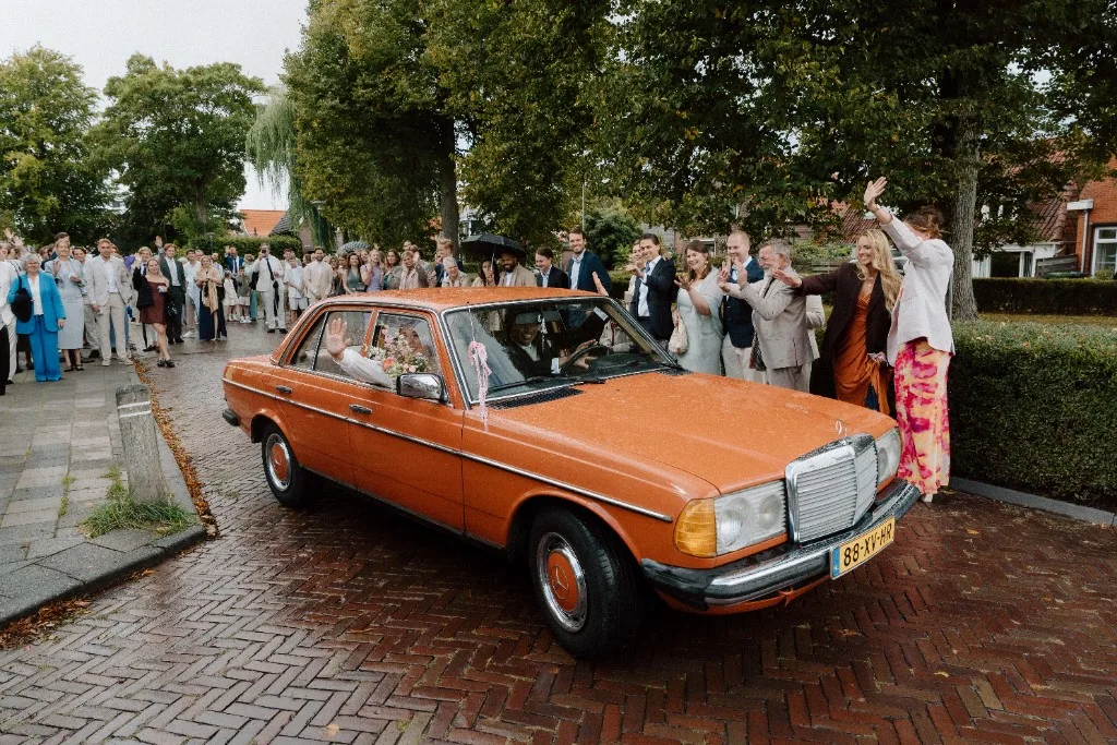Het bruidspaar vertrekt na de ceremonie; gasten zwaaien mee